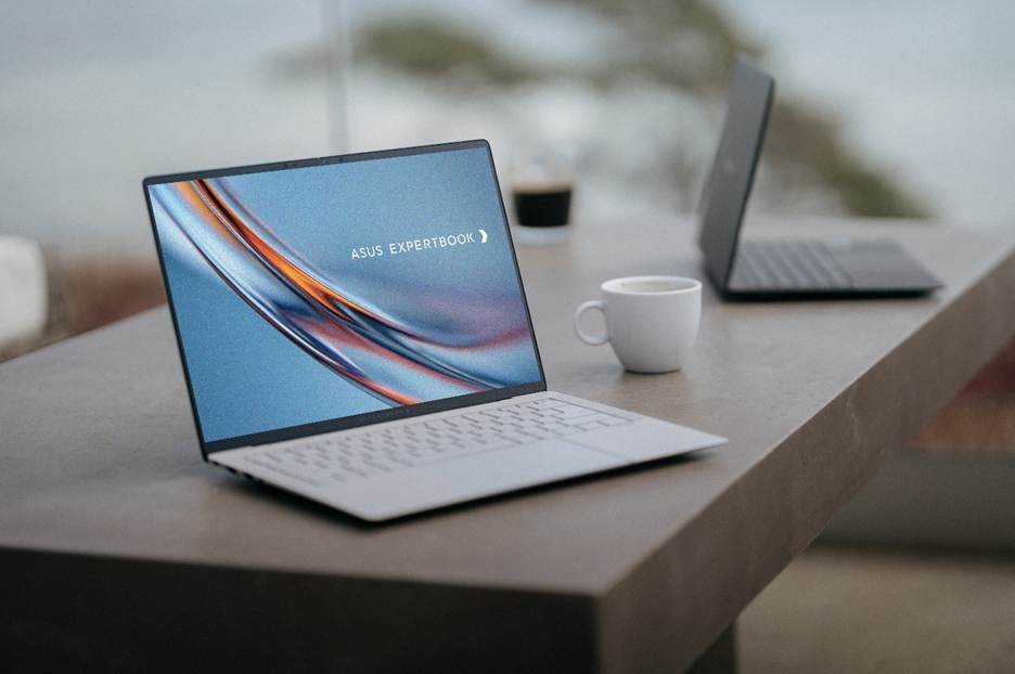 The image shows a sleek ASUS ExpertBook laptop placed on a wooden surface, with a cup of coffee on the desk and a clear view of the ocean in the background.

AI-generated content may be incorrect.